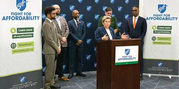 Randi Weingarten speaks at a podium as several other people stand besides her.