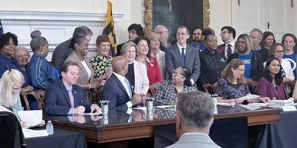 A group of people gather around a politician who is about to sign a bill. 