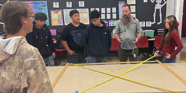 A group of students make a frame together using wood and tape.