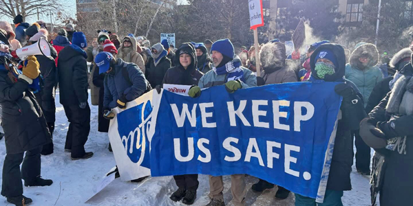 A group of protestors old up a sign in the winter that says "WE KEEP US SAFE".