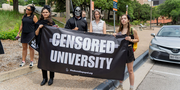 A group of protestors stand together holding a signs that reads "Censored University". A group of protestors stand together holding a signs that reads "Censored University".